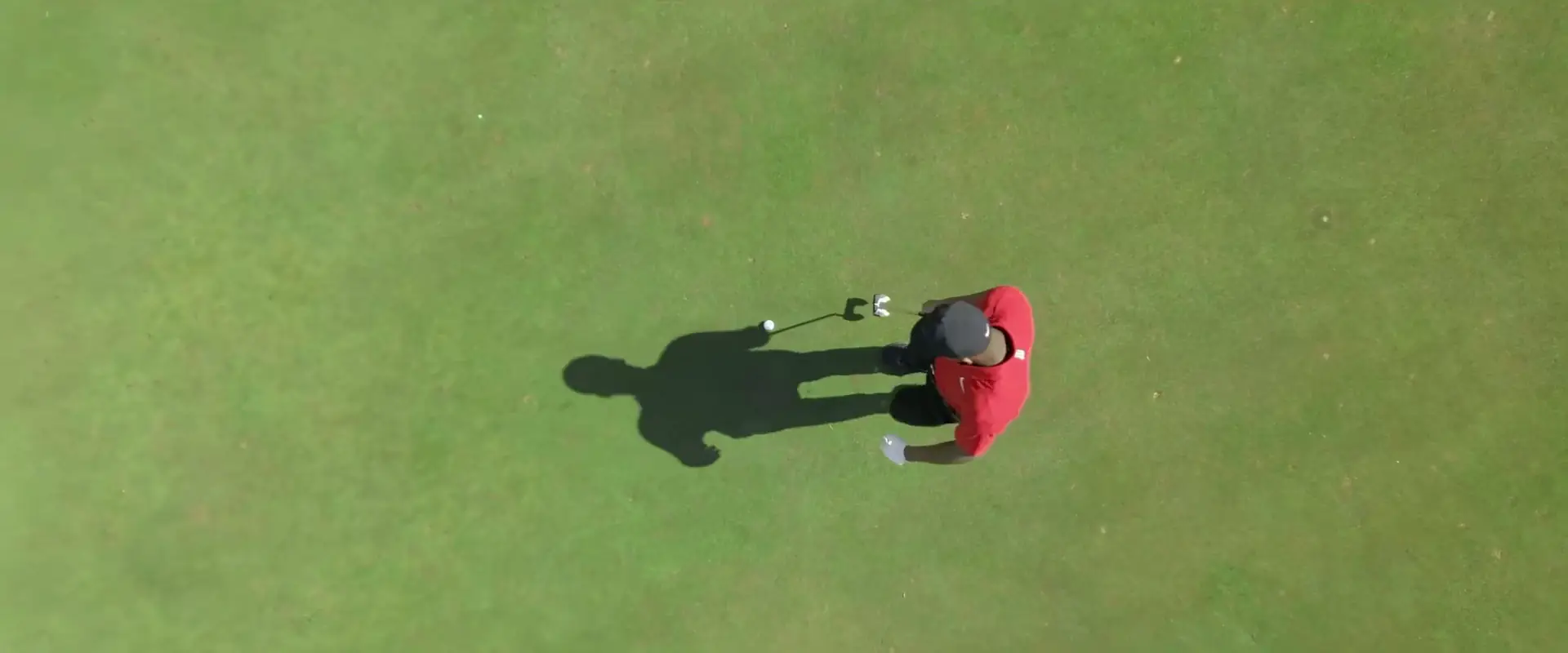 Un giovane golfista con la polo rossa visto dall'alto sul green, dallo spec commercial di Reelab Production (non affiliato a Nike Inc.)